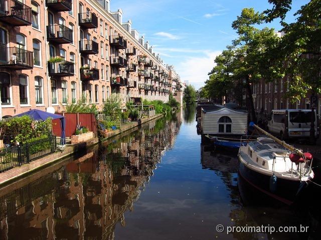 Lindo canal em Amsterdam refletindo o céu azul, com barcos tipo "casa" flutuante