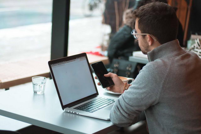 Homem utilizando notebook e smartphone